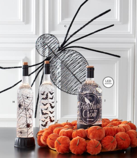 Decorative bottles with Halloween-themed designs on a table with pumpkins.