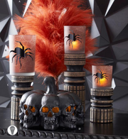 Halloween-themed candles with spider designs and decorative pumpkins on a geometric black background.