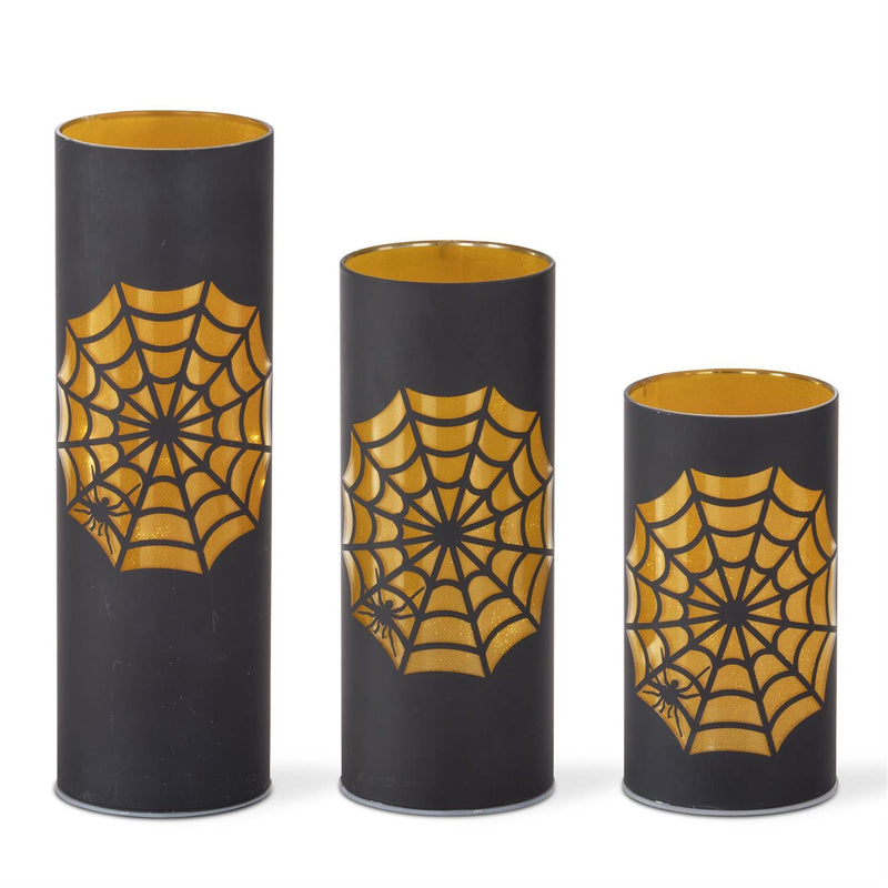 Three black cylindrical candles with gold spider web designs on a white background