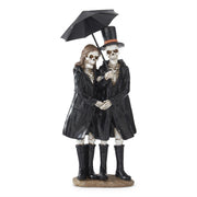 Statue of two skeletons in black coats and boots holding a black umbrella on a white background