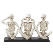 Three skeleton figurines in a 'see no evil, hear no evil, speak no evil' pose on a white background.
