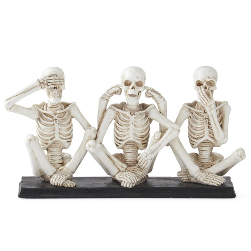 Three skeleton figurines in a 'see no evil, hear no evil, speak no evil' pose on a white background.