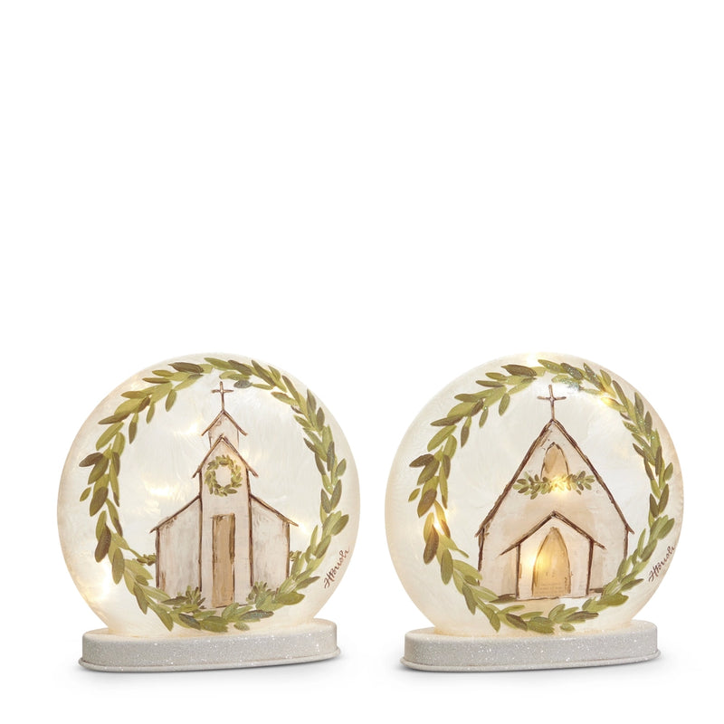 Two decorative glass globes with a church illustration and greenery on a white background