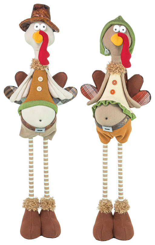 Two tall decorative turkey figurines with long striped legs and brown feet, shown side by side on a plain white background. One wears a cowboy hat and tan outfit, and the other wears a green hood and orange outfit.