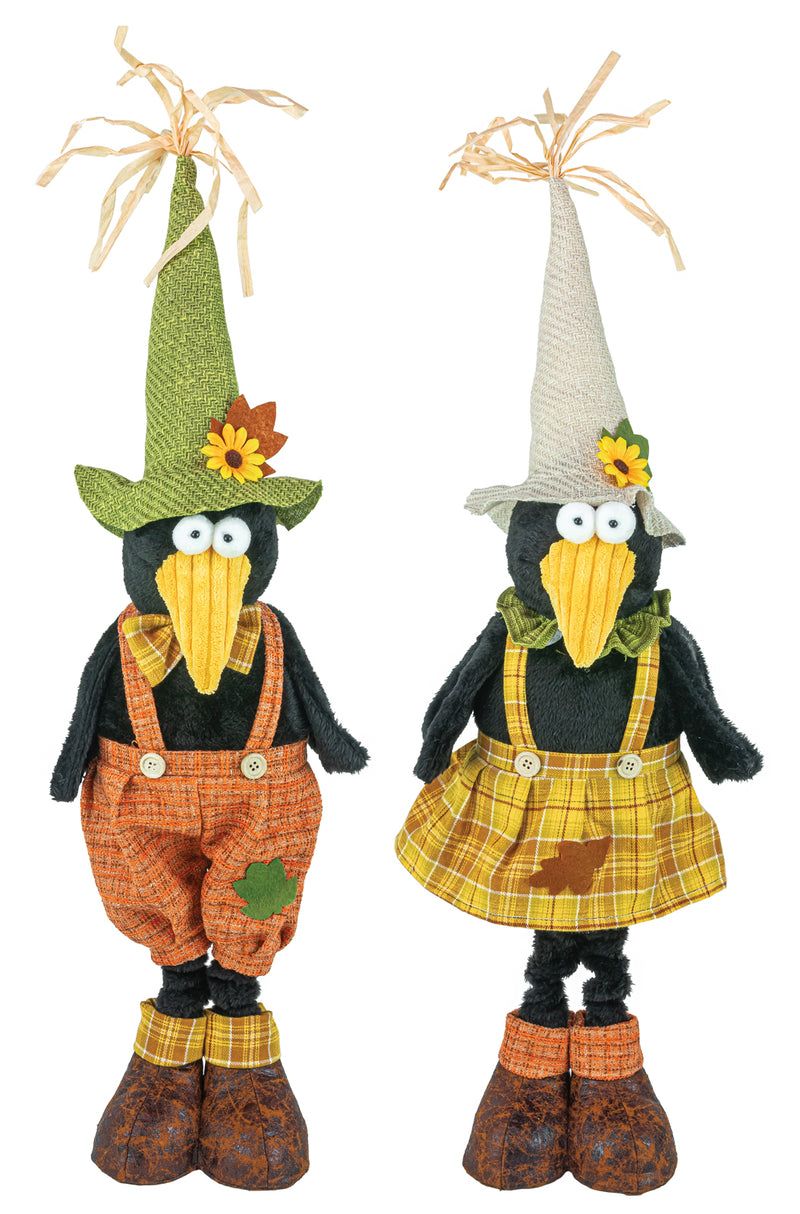 Two decorative scarecrow figurines side by side on a white background. The left scarecrow wears a green pointed hat with a yellow flower, orange plaid overalls, and brown shoes.