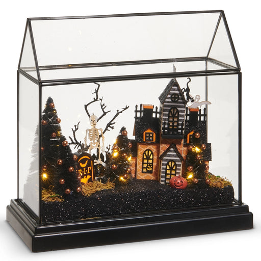 Halloween-themed diorama with a haunted house, trees, and skeleton in a glass display case.