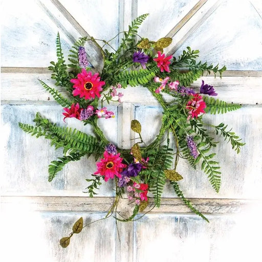 A decorative floral wreath with green ferns and bright pink, purple, and red flowers, displayed against a distressed white wooden door.