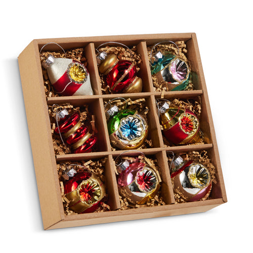 A set of vintage Christmas ornaments displayed in a cardboard box with compartments, containing various colorful glass balls.