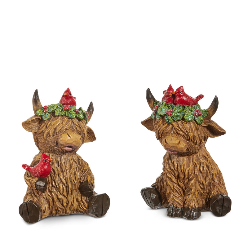 Two decorative Highland cow figurines with red birds and floral wreaths on a white background