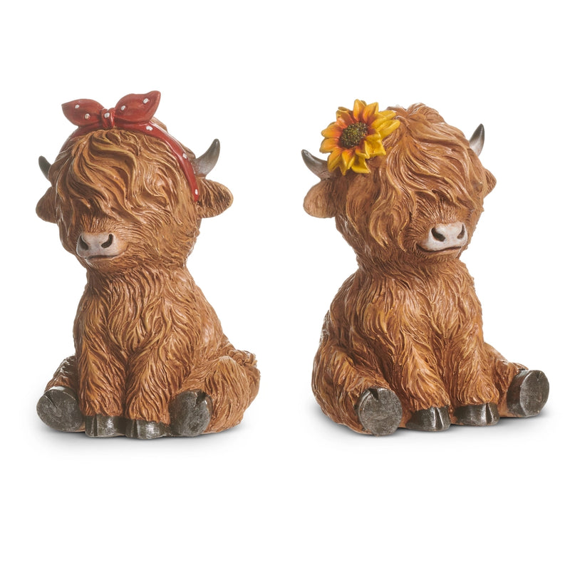 Two decorative Highland cow figurines with accessories on a white background