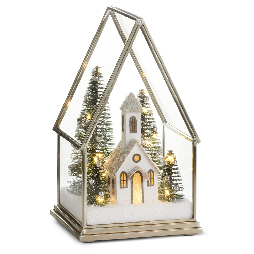 Decorative Christmas scene with a church, trees, and lights inside a glass terrarium on a white background.