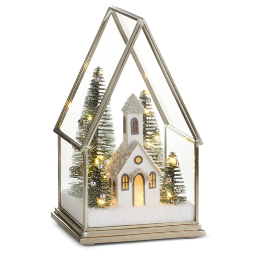 Decorative Christmas scene with a church, trees, and lights inside a glass terrarium on a white background.