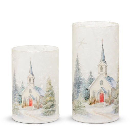 Two cylindrical candles with winter scene designs featuring churches and trees on a white background.