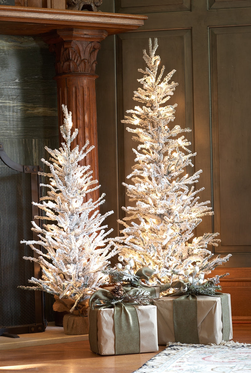 Two illuminated Christmas trees with presents underneath in a room setting.