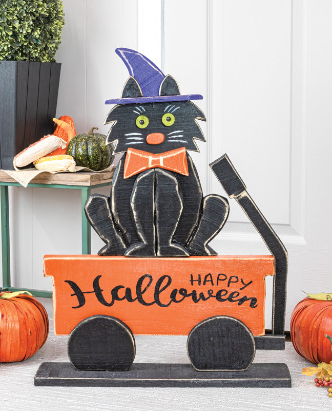 Halloween-themed decorative cat in a wagon with pumpkins and autumn leaves.