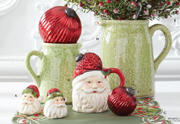 Decorative Christmas items including a Santa figure, red ornaments, and green pitchers on a table.