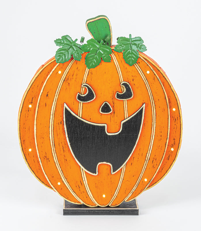 A decorative jack-o'-lantern pumpkin sign with a carved face, green leaves, and a small black base, photographed against a plain light background.