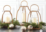 Decorative setup with gold lanterns, candles, and greenery on a white background