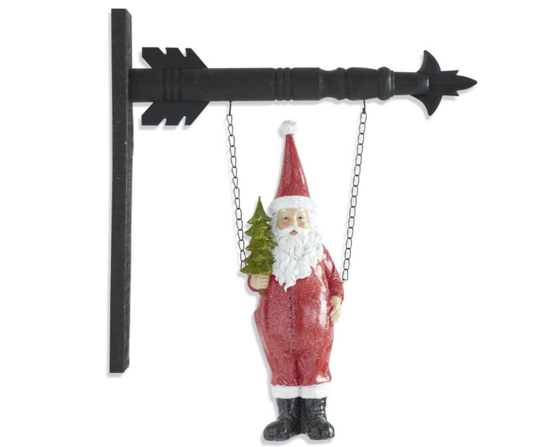 Decorative figure of a Santa Claus holding a small tree, hanging from a black arrow-shaped stand on a white background.