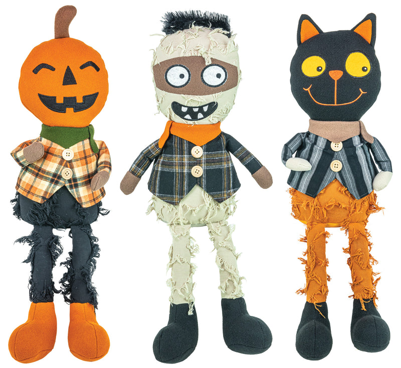 Three Halloween plush toys standing side by side on a white background: a jack-o'-lantern doll with an orange pumpkin head, a mummy doll with beige bandages and a plaid shirt, and a black cat doll with yellow eyes and orange pants.