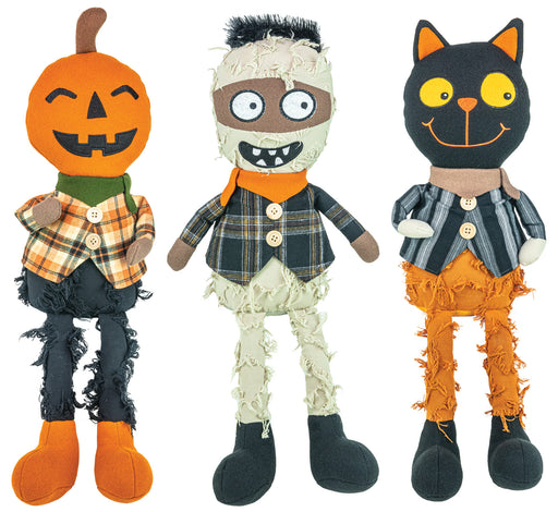 Three Halloween plush toys standing side by side on a white background: a jack-o'-lantern doll with an orange pumpkin head, a mummy doll with beige bandages and a plaid shirt, and a black cat doll with yellow eyes and orange pants.