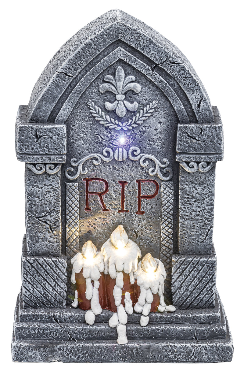 A gothic-style Halloween tombstone decoration with a faux-stone gray surface, illuminated LED lights, and three white wax-dripping candles at the base. The front features the letters 'RIP' in red.