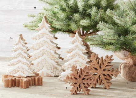 Decorative Christmas trees and snowflakes on a wooden surface with a Christmas tree in the background.