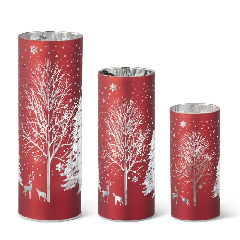 Three red cylindrical candles with white tree and deer designs on a white background