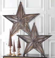 Two large star-shaped decorative items on a table with a white paneled wall background.