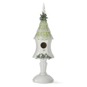 A white and green glittered birdhouse with a pedestal, decorated with holly and a snowflake-like pattern on the sides.