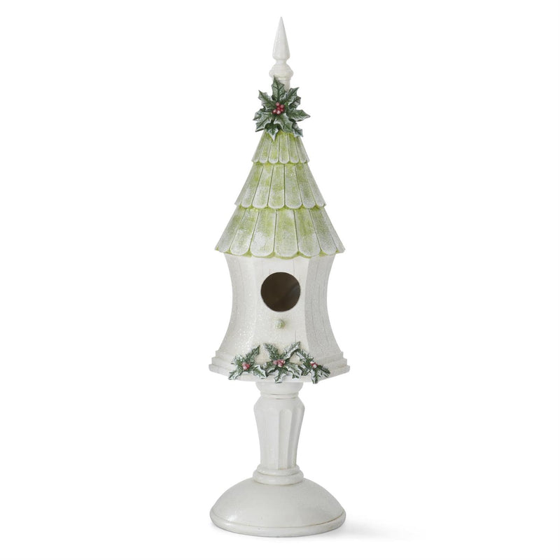 A white and green glittered birdhouse with a pedestal, decorated with holly and a snowflake-like pattern on the sides.
