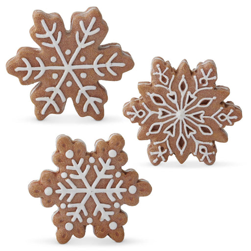 A set of three gingerbread snowflake-shaped figurines with white icing details on a white background.
