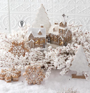 Decorative scene with gingerbread cookies shaped like snowflakes and a small village model on a textured white background.