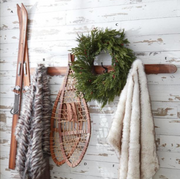 Decorative wall with skis, snowshoes, and a wreath on hooks against a wooden wall.