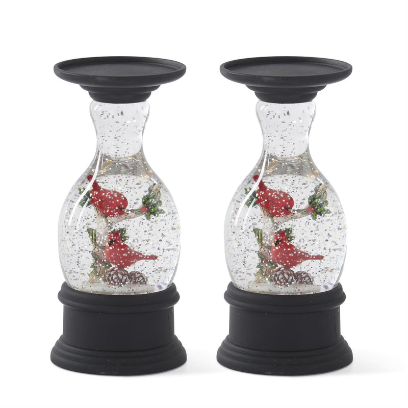 Two decorative candle holders with snow globe effect and cardinal birds on a white background