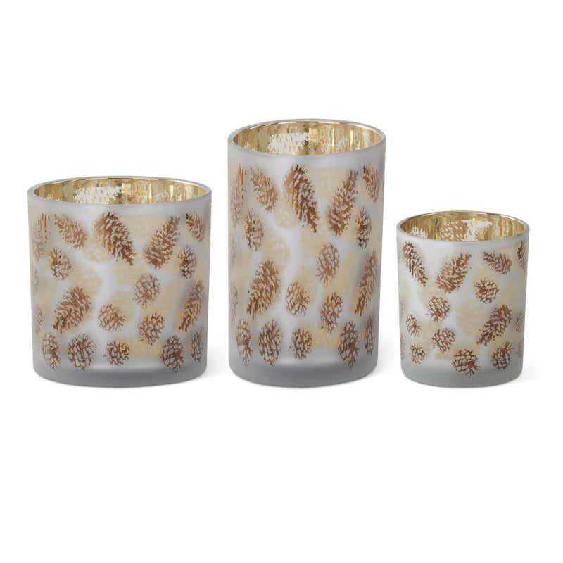 Three decorative candle holders with gold pine cone patterns on a white background