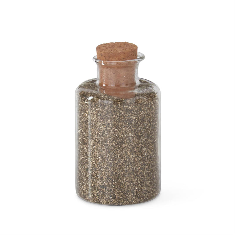 A cylindrical glass jar with gold glitter sand, topped with a cork stopper.