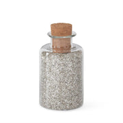 A glass jar filled with silver glitter sand, topped with a cork stopper.