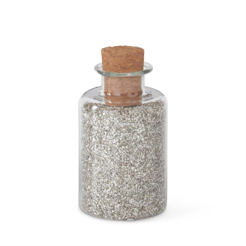 A glass jar filled with silver glitter sand, topped with a cork stopper.