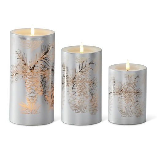 Three silver candles with pine branch designs on a white background