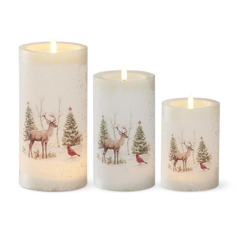 Set of three Christmas-themed candles with deer and tree designs on a white background
