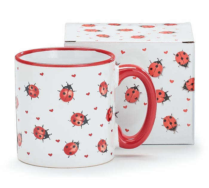 A white ceramic mug with a red handle and red rim, decorated with a pattern of red ladybugs and small red hearts, shown in front of its matching white box with the same print.