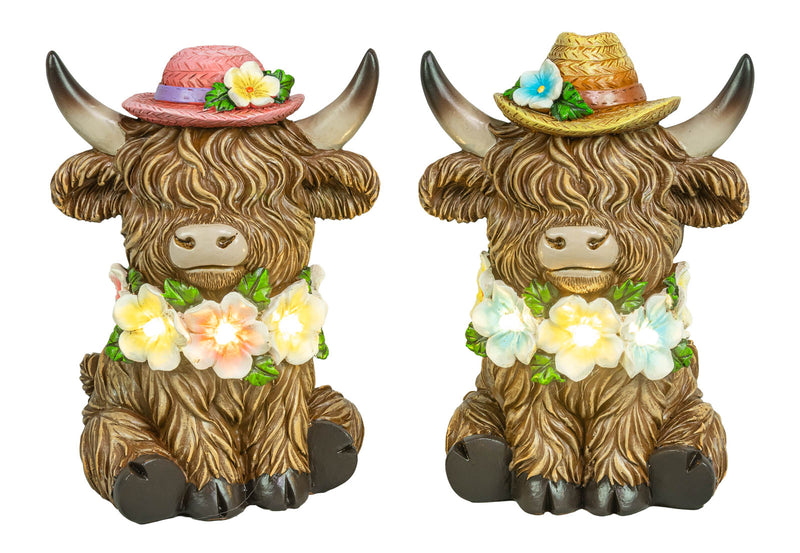Two decorative Highland cow figurines with long shaggy brown fur, wearing floral leis and straw hats, shown side by side on a plain white background.