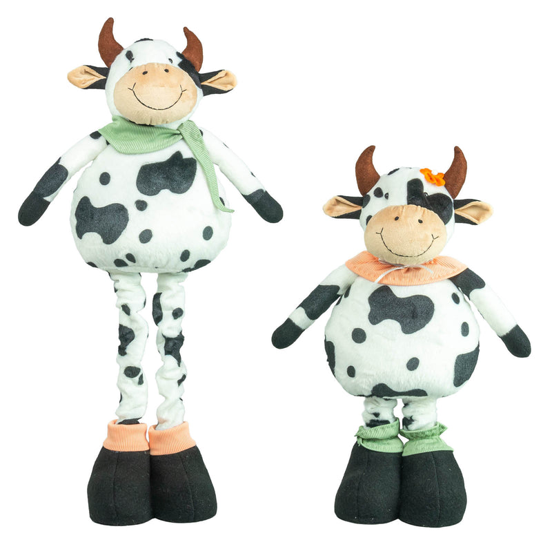 Two cow-shaped plush toys on a plain white background, one tall and one short, both with black-and-white spotted bodies, brown horns, smiling faces, and different colored neck scarves and hooves.