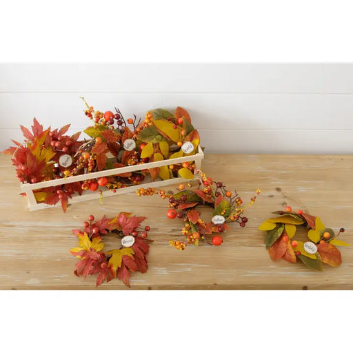 Decorative fall-themed wreaths and arrangements on a wooden surface with a white background