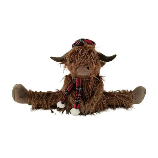A brown shaggy Highland cow plush toy sitting cross-legged, wearing a red and black tartan plaid hat and matching scarf with white pom-poms, on a solid white background.