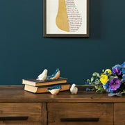 Decorative setup with birds on books and flowers on a wooden surface against a dark blue wall.