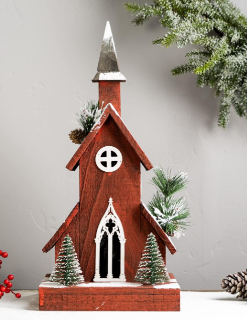 Decorative model of a red church with white accents, surrounded by Christmas trees and decorations on a light gray background.