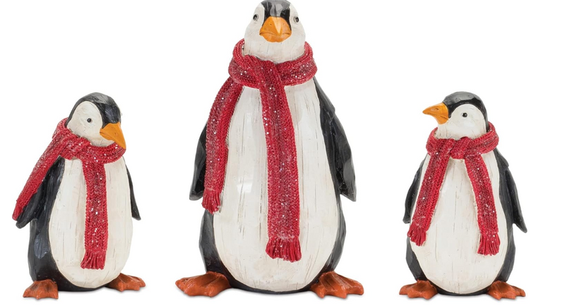 Three penguin figurines wearing red scarves on a white background