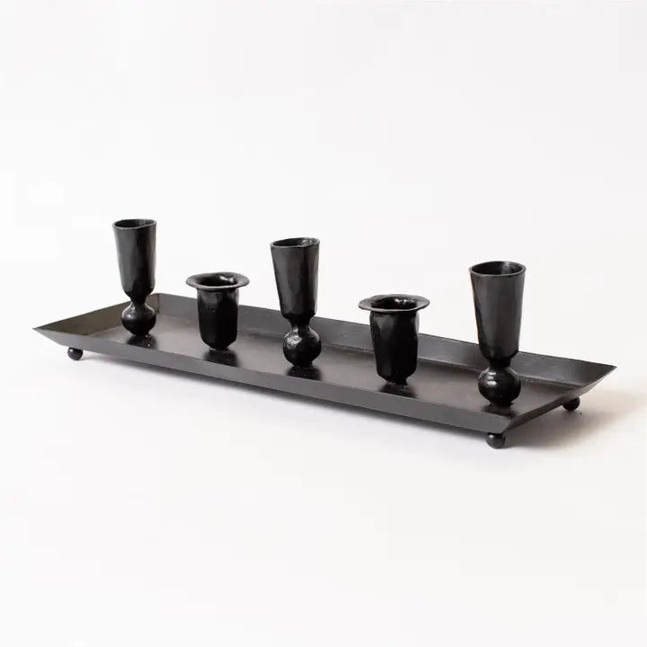 Black metal candle holder tray with five cylindrical candles on a white background